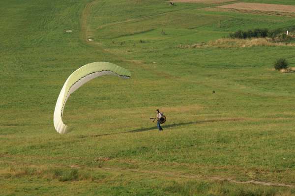 pilot i opadające skrzydło paralotni po lądowaniu